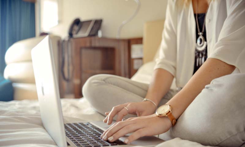 woman sitting on her bed typing on laptop