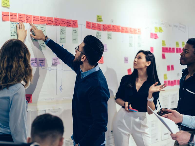 Team of multicultural young people pointing on wall with glued colorful paper notes