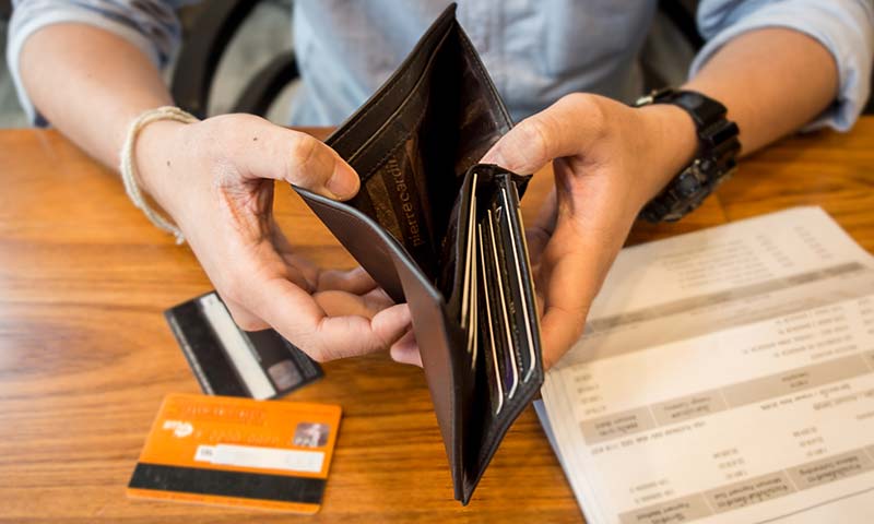 debt A close-up shot of a man holding open his empty wallet. On the table below the wallet are a few credit cards and a bank statement.