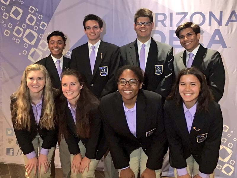 Four boys and four girls posing in front of a DECA AZ banner. They are all smiling and wearing dark blue blazers.