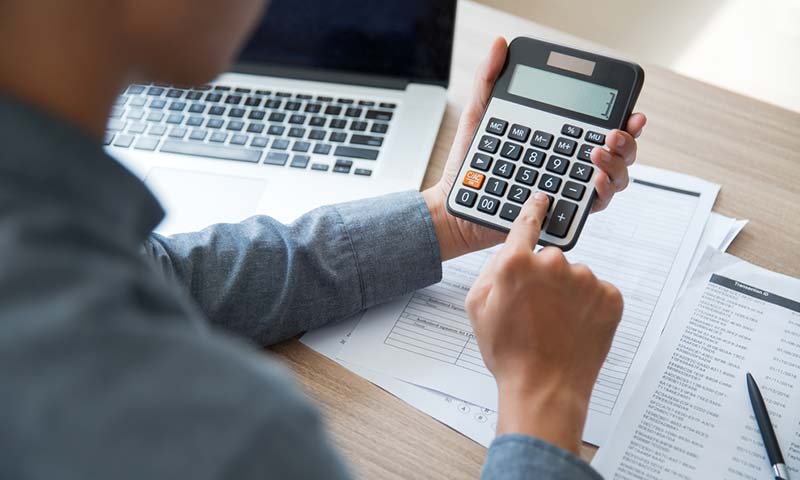 calculating A man at his desk with a laptop and various paperwork. He is usinga calculator to figure out his finances.
