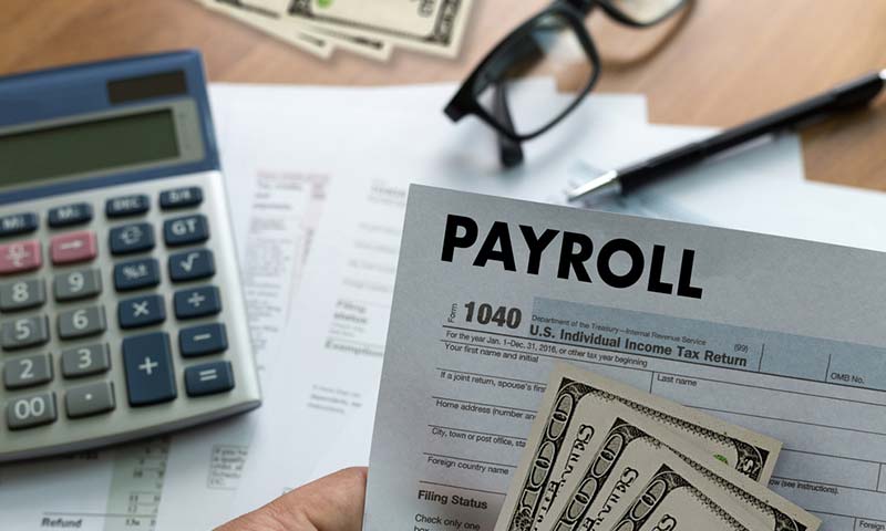 A payroll sheet with money and a calculator in the background