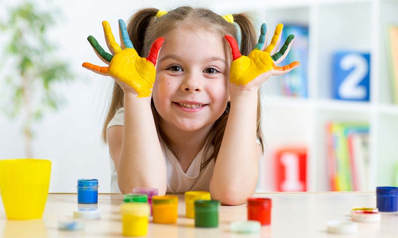 A happy child at daycare with finger paint all over her palms