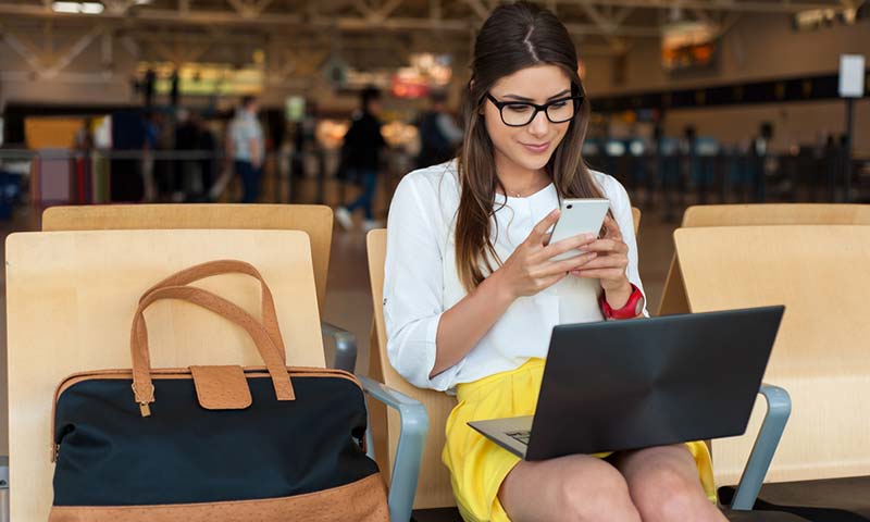A woman sitting at the airport using her laptop and smart phone