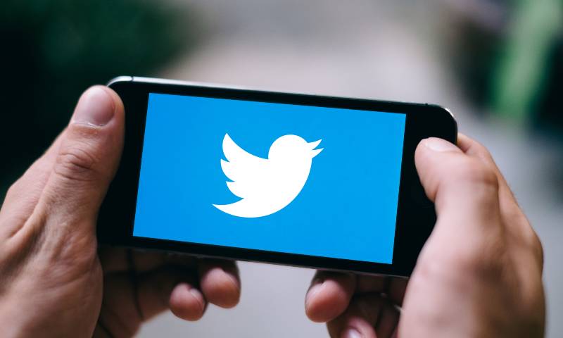 Close up of a man holding his cell phone, twitter logo of a bird on the screen