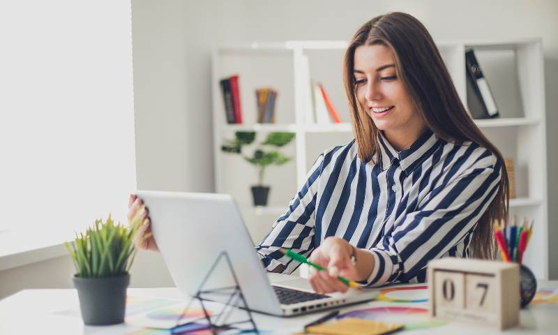 Young lady working at her desk, open laptop and various papers spread about