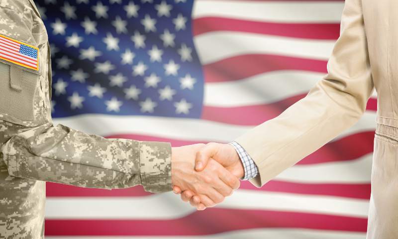 Solider in uniform shaking the hand of a business man, American flag in background
