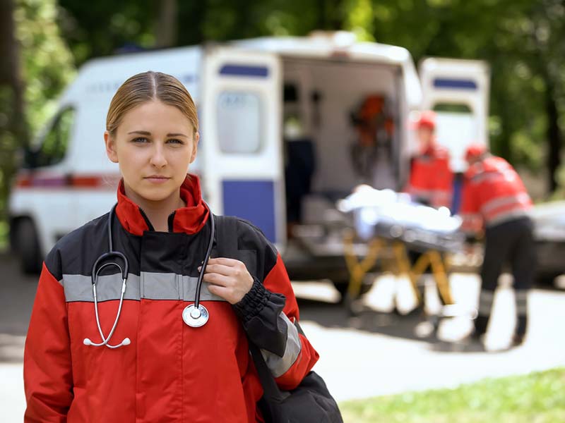 Female ambulance driver looking stern while two other paramedics load someone into the ambulance