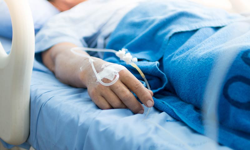 Person in hospital bed with IV in their hand