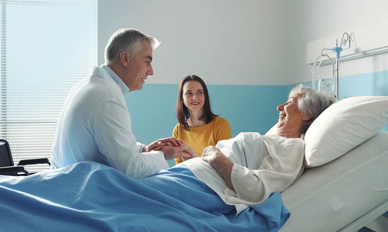 Doctor sitting bedside with elderly patient and her daughter
