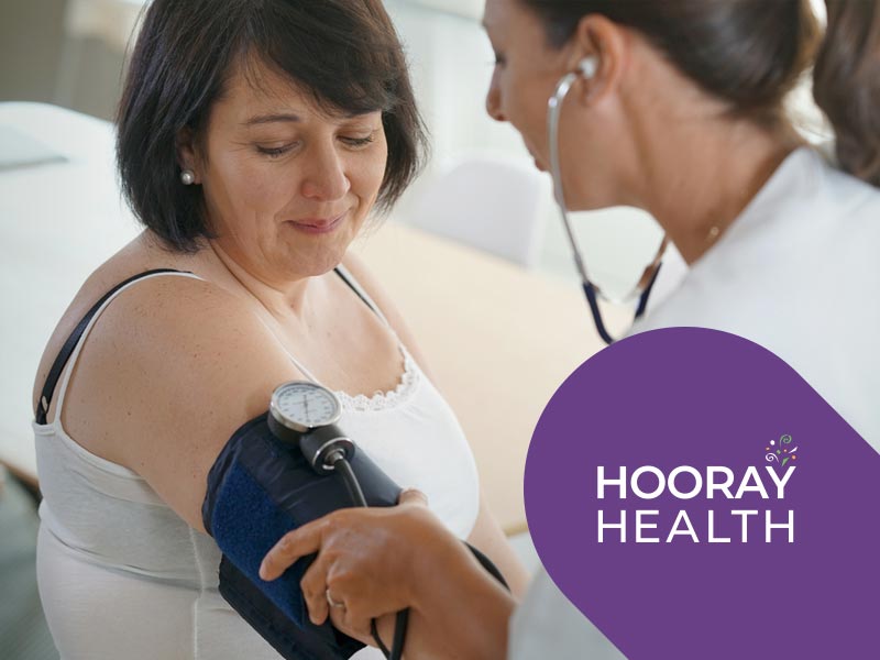 Doctor checking patient's blood pressure. Hooray Health logo.