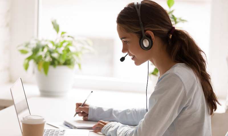 Side view of a young lady wearing a headset, looking at her laptop, working