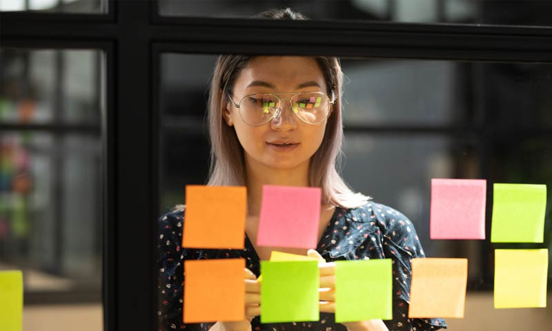 A woman using sticky notes on a glass board to do her planning