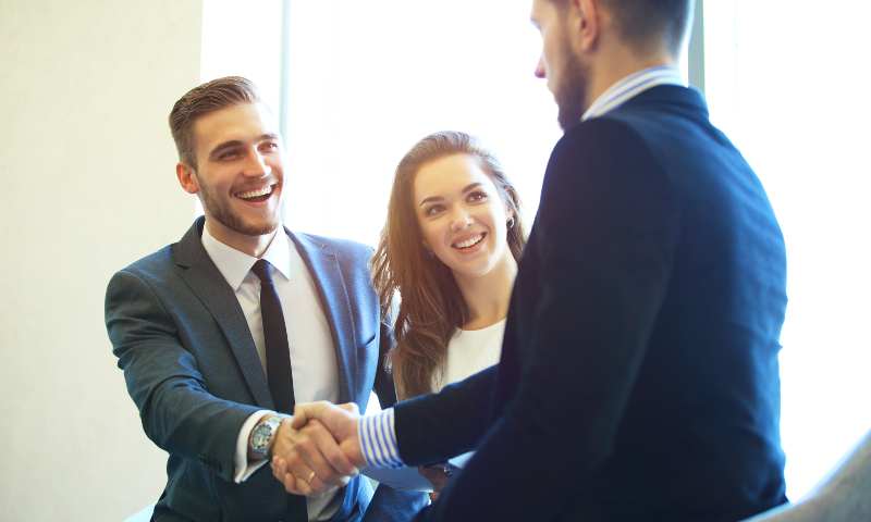Business men shaking hands, woman smiling between them