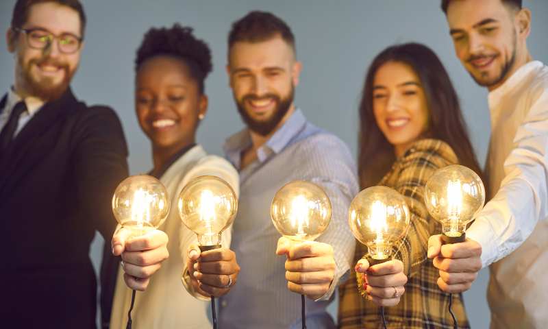 Happy people holding out a lit up lightbulb