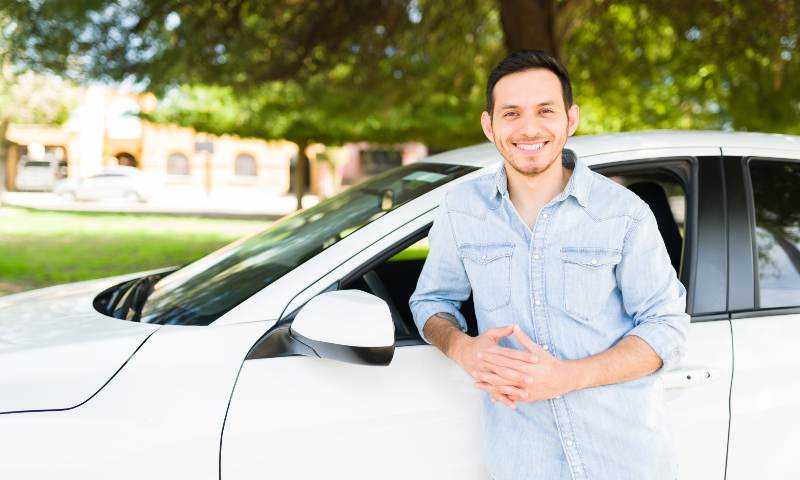 Man smiling, leaning up against car.