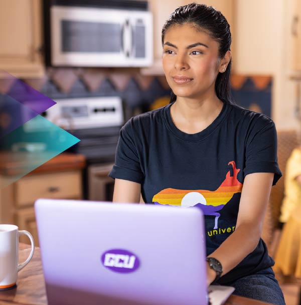 Young woman in a kitchen working on a laptop with a CGU logo on it.