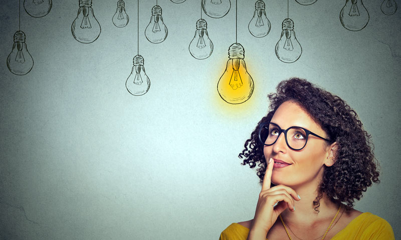 Woman with glasses and finger held to lips is looking up at a drawing of a yellow light bulb which is different than the other lights