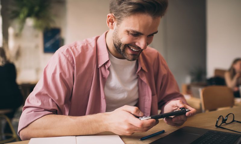 Happy hipster guy enjoying time for playing virtual 3d via nintendo console joystick during break time, smiling male gamer passing next level via handheld joypad app