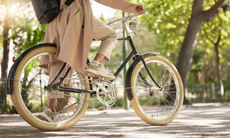 Bicycle, closeup and feet of casual cyclist travel on a bike in a park outdoors in nature for a ride or commuting. Exercise, wellness and lifestyle student cycling as sustainable transport.